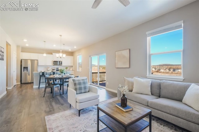 living room featuring ceiling fan with notable chandelier and light hardwood / wood-style flooring