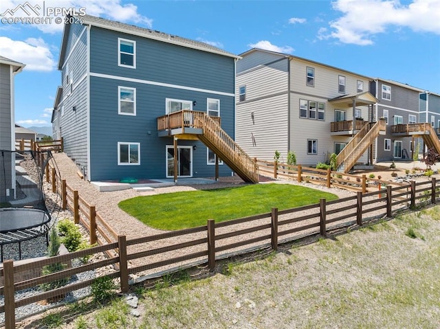 rear view of house featuring a trampoline, a wooden deck, a yard, and a patio