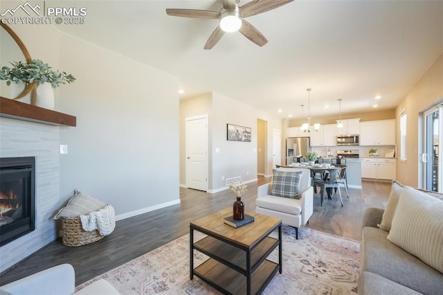 living room featuring hardwood / wood-style flooring, ceiling fan, and a tiled fireplace