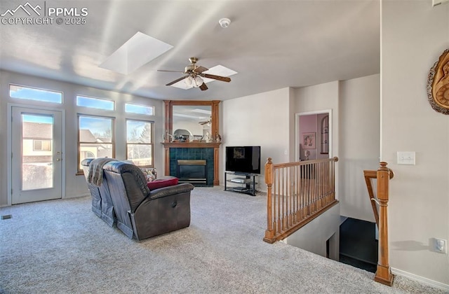 carpeted living room with a skylight, a tiled fireplace, and ceiling fan