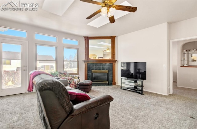 living room with ceiling fan, a skylight, light carpet, and a tiled fireplace