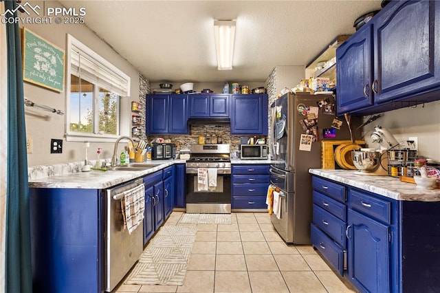 kitchen with sink, blue cabinets, light tile patterned floors, and appliances with stainless steel finishes