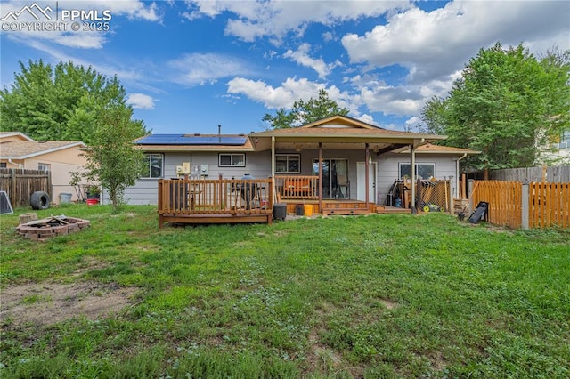 back of house with an outdoor fire pit, solar panels, a lawn, and a wooden deck