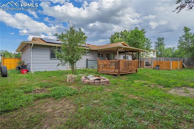 back of property with solar panels, an outdoor fire pit, a lawn, and a wooden deck