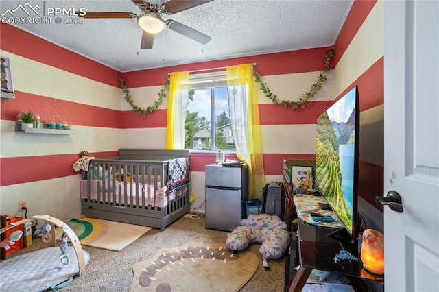 carpeted bedroom featuring a crib, a textured ceiling, ceiling fan, and stainless steel fridge