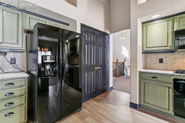 kitchen with light hardwood / wood-style floors, backsplash, light stone counters, and black appliances