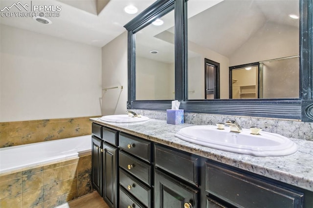 bathroom featuring lofted ceiling, vanity, and tiled bath