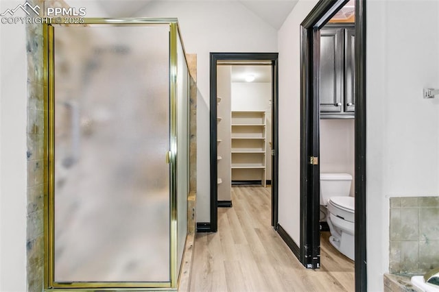 bathroom with wood-type flooring, vaulted ceiling, toilet, and walk in shower