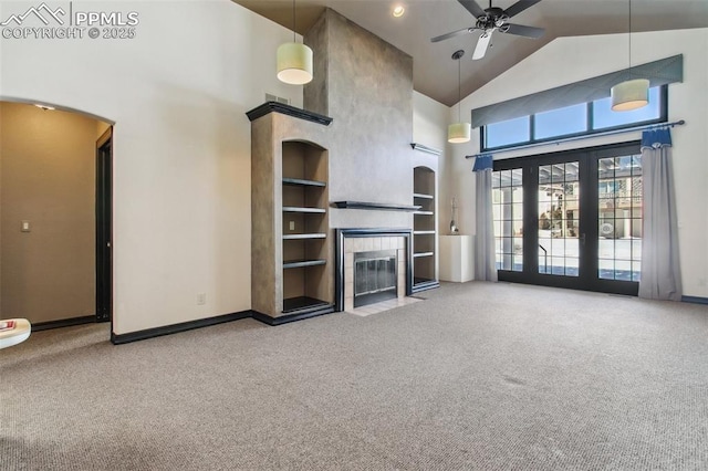 unfurnished living room featuring built in features, a tile fireplace, high vaulted ceiling, carpet flooring, and french doors