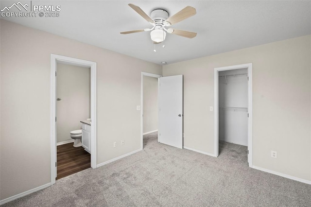 unfurnished bedroom featuring a closet, light carpet, ensuite bath, ceiling fan, and a walk in closet