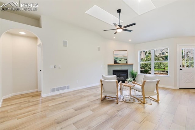 sitting room featuring ceiling fan, vaulted ceiling with skylight, and light hardwood / wood-style floors