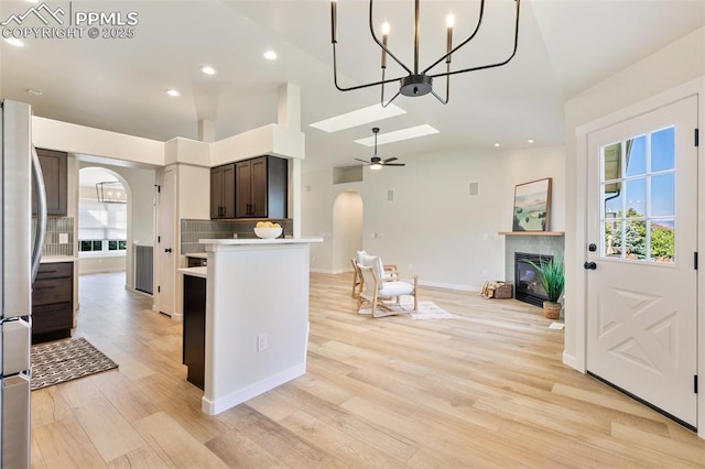 kitchen with dark brown cabinetry, light hardwood / wood-style floors, ceiling fan, stainless steel refrigerator, and high vaulted ceiling