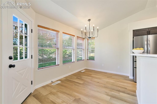 unfurnished dining area featuring a chandelier, lofted ceiling, and light hardwood / wood-style flooring