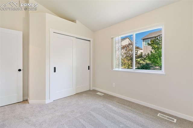 unfurnished bedroom with lofted ceiling, a closet, and light carpet