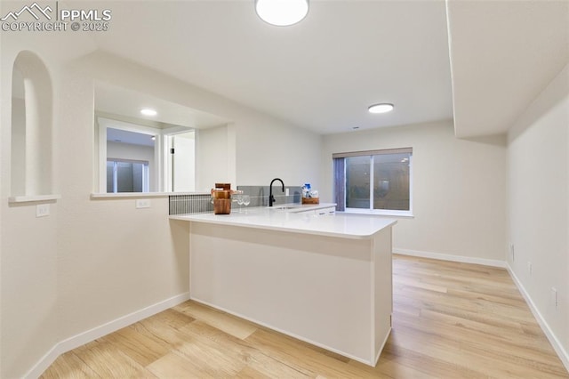 kitchen featuring light wood-type flooring, kitchen peninsula, and sink