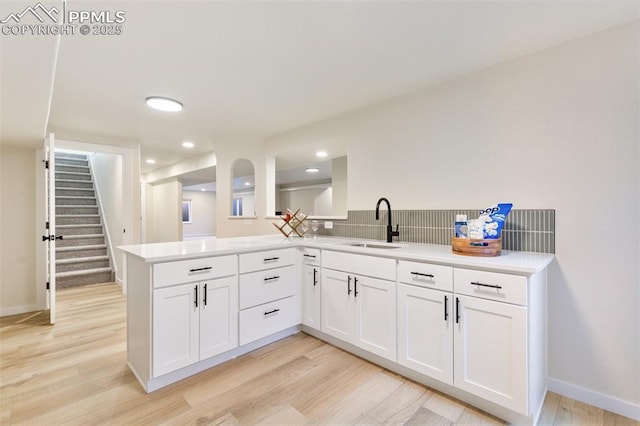 kitchen with light wood-type flooring, kitchen peninsula, sink, and white cabinetry