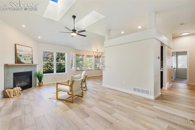 living area featuring light wood-type flooring, a tiled fireplace, ceiling fan with notable chandelier, and vaulted ceiling with skylight