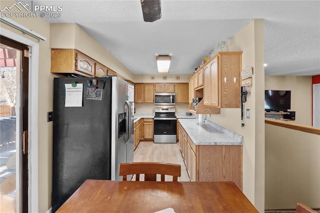 kitchen with appliances with stainless steel finishes, light brown cabinets, a textured ceiling, and light hardwood / wood-style floors