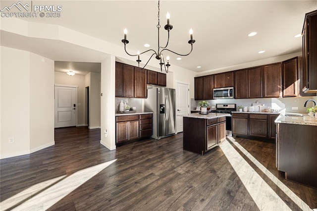 kitchen with stainless steel appliances, a notable chandelier, dark wood-type flooring, light stone counters, and a center island