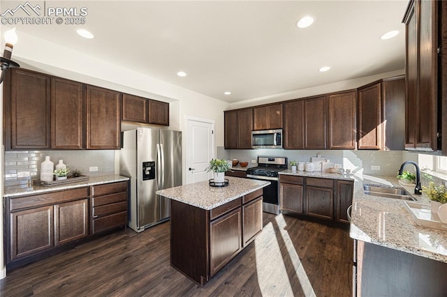 kitchen featuring dark brown cabinetry, a kitchen island, dark wood-type flooring, stainless steel appliances, and sink