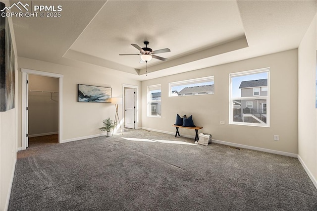 empty room with a raised ceiling, ceiling fan, and dark colored carpet