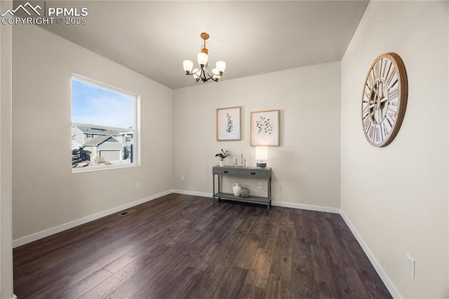 spare room with dark wood-type flooring and a notable chandelier