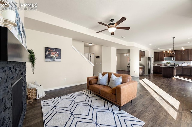 living room with a fireplace, dark wood-type flooring, and ceiling fan with notable chandelier