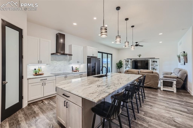 kitchen featuring black appliances, an island with sink, white cabinetry, and wall chimney exhaust hood