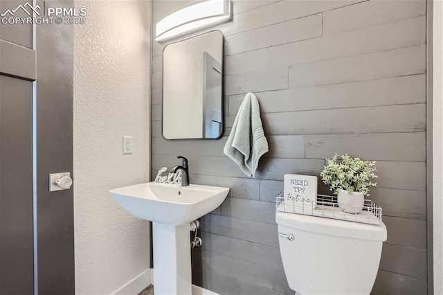 bathroom with sink, wooden walls, and toilet