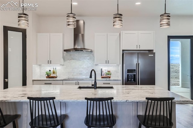 kitchen with decorative light fixtures, high end fridge, white cabinets, and wall chimney exhaust hood