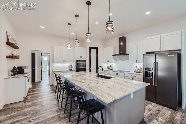 kitchen with white cabinetry, an island with sink, sink, black appliances, and wall chimney exhaust hood