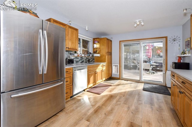 kitchen with stainless steel appliances, sink, backsplash, and light hardwood / wood-style flooring