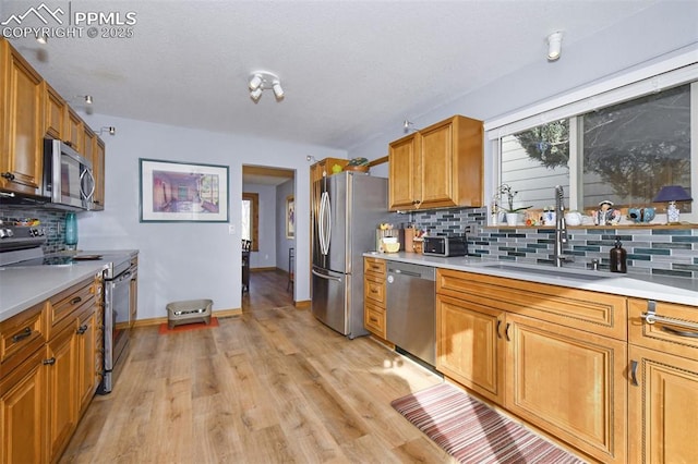 kitchen featuring appliances with stainless steel finishes, light hardwood / wood-style floors, backsplash, and sink