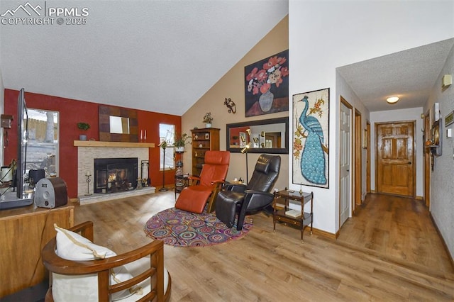 living room with a textured ceiling, light wood-type flooring, vaulted ceiling, and a stone fireplace