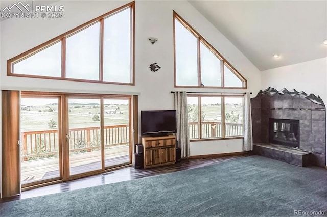 unfurnished living room with a tiled fireplace, plenty of natural light, and a high ceiling