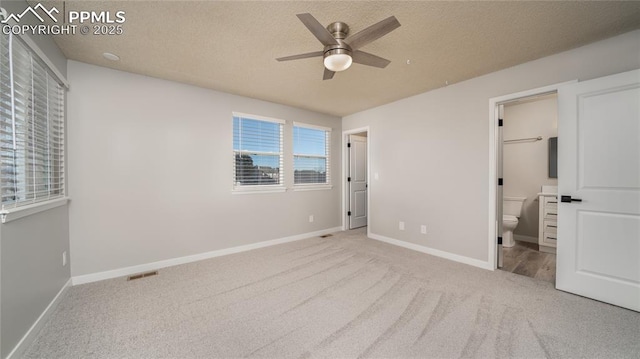 unfurnished bedroom with ensuite bath, light colored carpet, ceiling fan, and a textured ceiling