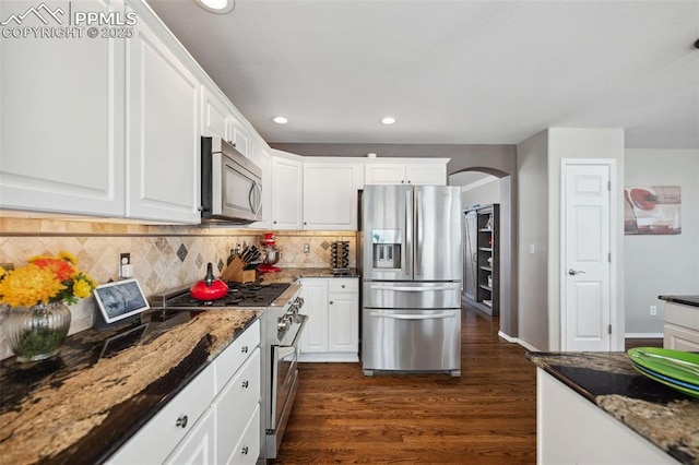 kitchen with backsplash, white cabinets, stainless steel appliances, and dark stone countertops