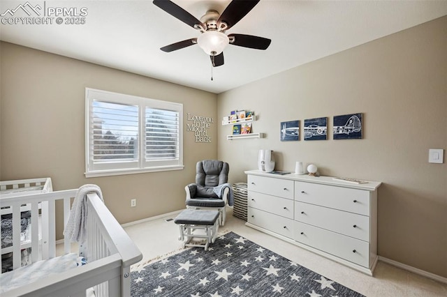 bedroom featuring a nursery area, light colored carpet, and ceiling fan