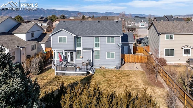 rear view of house with a deck with mountain view and a lawn