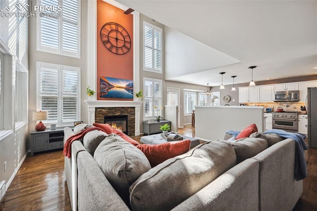 living room featuring dark wood-type flooring, a towering ceiling, and a stone fireplace