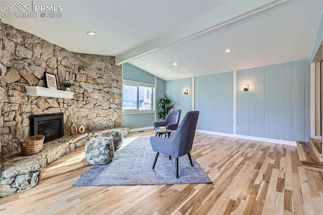 living room with light hardwood / wood-style floors, a stone fireplace, and lofted ceiling with beams