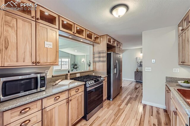 kitchen featuring a textured ceiling, light brown cabinets, stainless steel appliances, light stone counters, and light hardwood / wood-style flooring