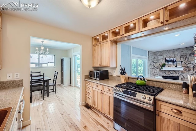 kitchen featuring a stone fireplace, stainless steel appliances, hanging light fixtures, a chandelier, and light hardwood / wood-style flooring