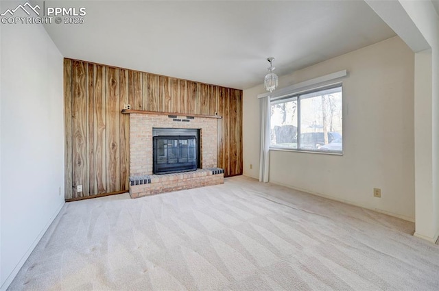 unfurnished living room featuring a notable chandelier, light colored carpet, wood walls, and a fireplace