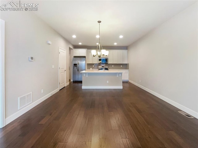 kitchen featuring backsplash, hanging light fixtures, appliances with stainless steel finishes, an island with sink, and dark hardwood / wood-style flooring