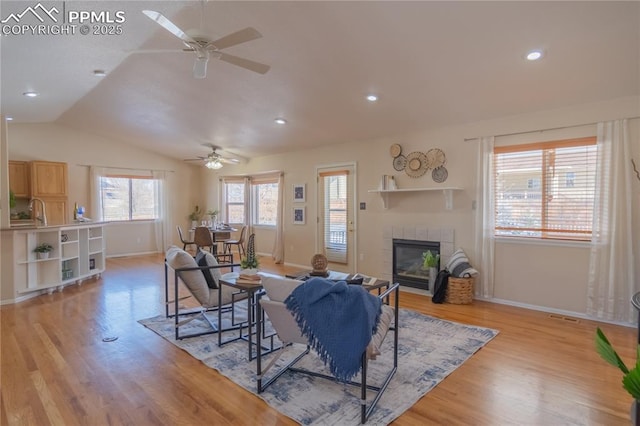 living room with ceiling fan, light hardwood / wood-style floors, vaulted ceiling, and a fireplace