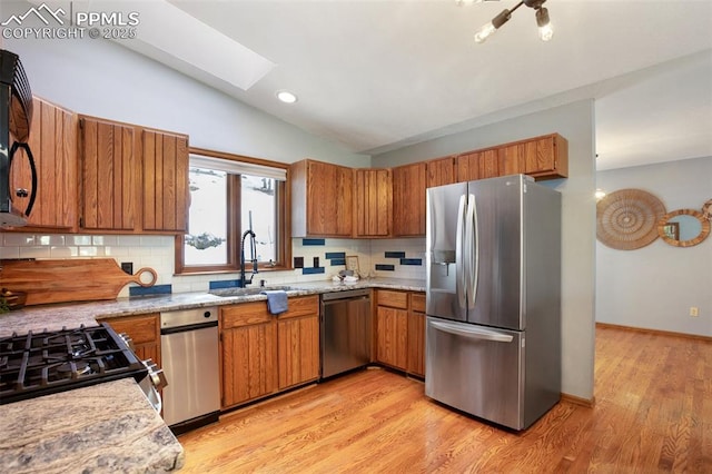 kitchen with sink, light hardwood / wood-style flooring, lofted ceiling with skylight, stainless steel appliances, and tasteful backsplash