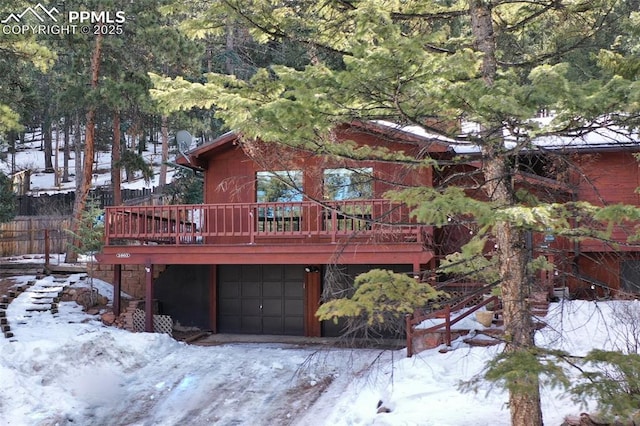 snow covered back of property with a wooden deck and a garage