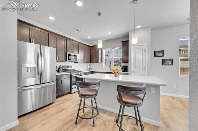 kitchen featuring appliances with stainless steel finishes, dark brown cabinetry, a kitchen island, a kitchen breakfast bar, and hanging light fixtures