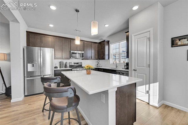 kitchen with light hardwood / wood-style floors, a kitchen island, hanging light fixtures, appliances with stainless steel finishes, and a kitchen breakfast bar